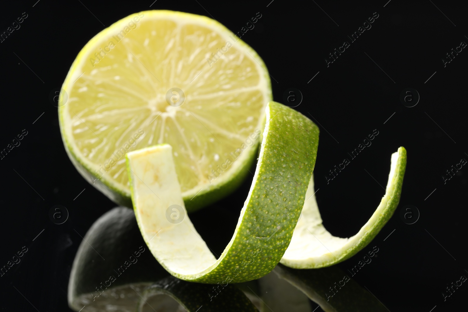 Photo of Fresh lime peel and half of fruit on black glass surface, closeup