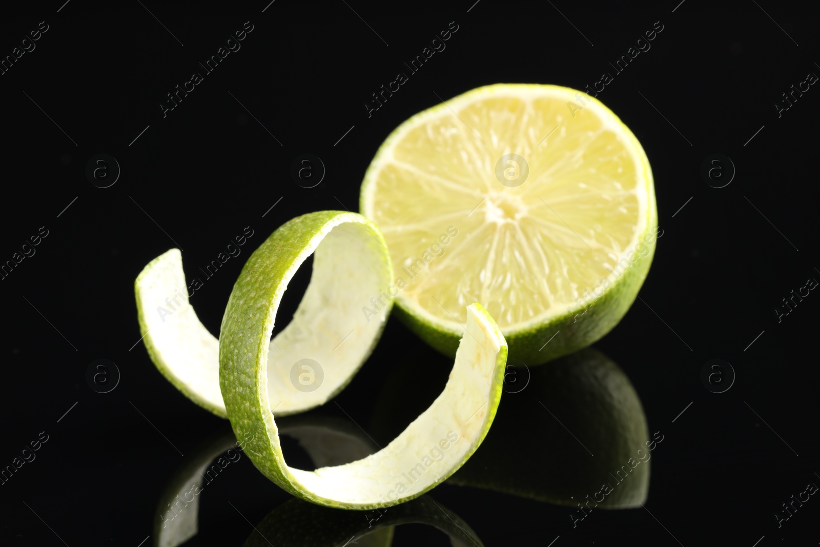 Photo of Fresh lime peel and half of fruit on black glass surface, closeup