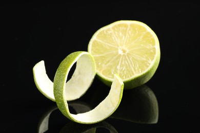 Photo of Fresh lime peel and half of fruit on black glass surface, closeup