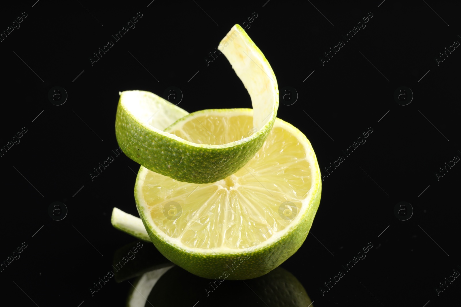 Photo of Fresh lime peel and half of fruit on black glass surface, closeup