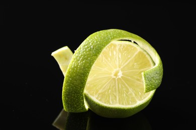 Photo of Fresh lime peel and half of fruit on black glass surface, closeup