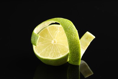 Photo of Fresh lime peel and half of fruit on black glass surface, closeup