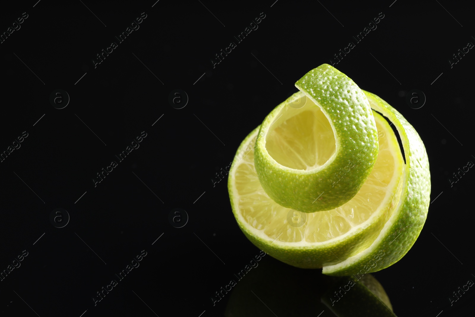 Photo of Fresh lime peel and half of fruit on black glass surface, closeup. Space for text