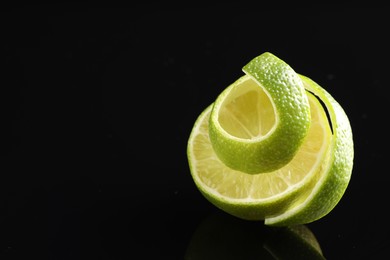 Photo of Fresh lime peel and half of fruit on black glass surface, closeup. Space for text