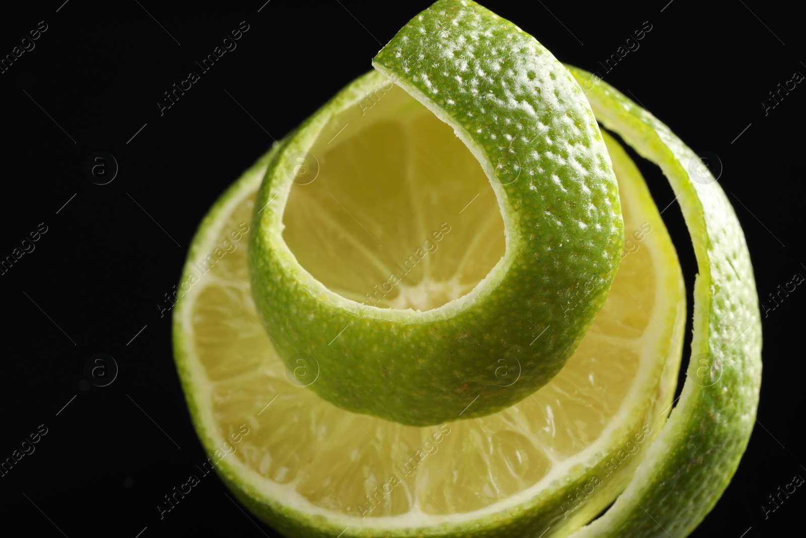 Photo of Fresh lime peel and half of fruit on black background, closeup