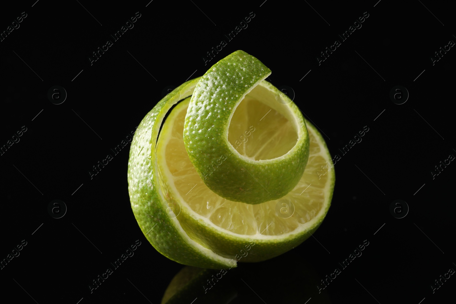 Photo of Fresh lime peel and half of fruit on black glass surface, closeup