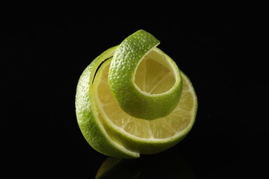 Photo of Fresh lime peel and half of fruit on black glass surface, closeup