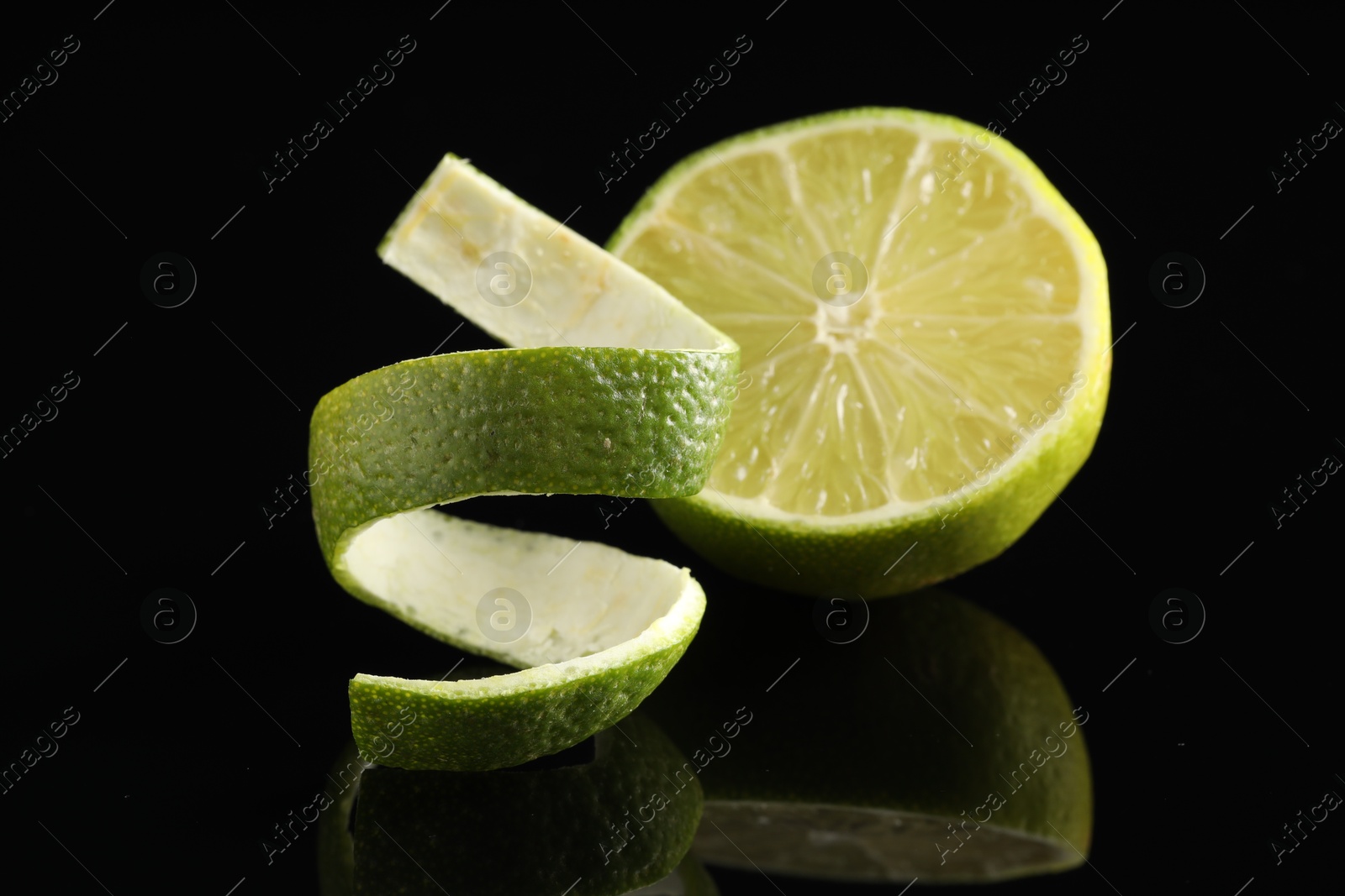 Photo of Fresh lime peel and half of fruit on black glass surface, closeup