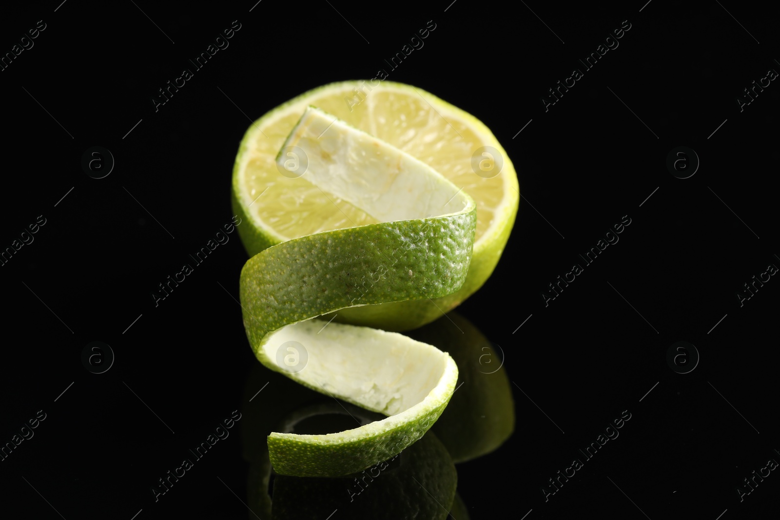 Photo of Fresh lime peel and half of fruit on black glass surface, closeup