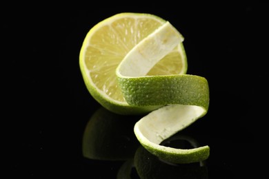 Photo of Fresh lime peel and half of fruit on black glass surface, closeup