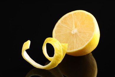 Photo of Fresh lemon peel and half of fruit on black glass surface, closeup