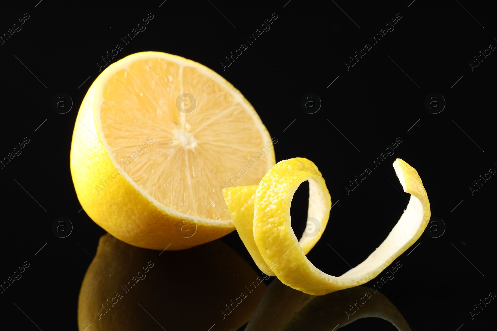 Photo of Fresh lemon peel and half of fruit on black glass surface, closeup