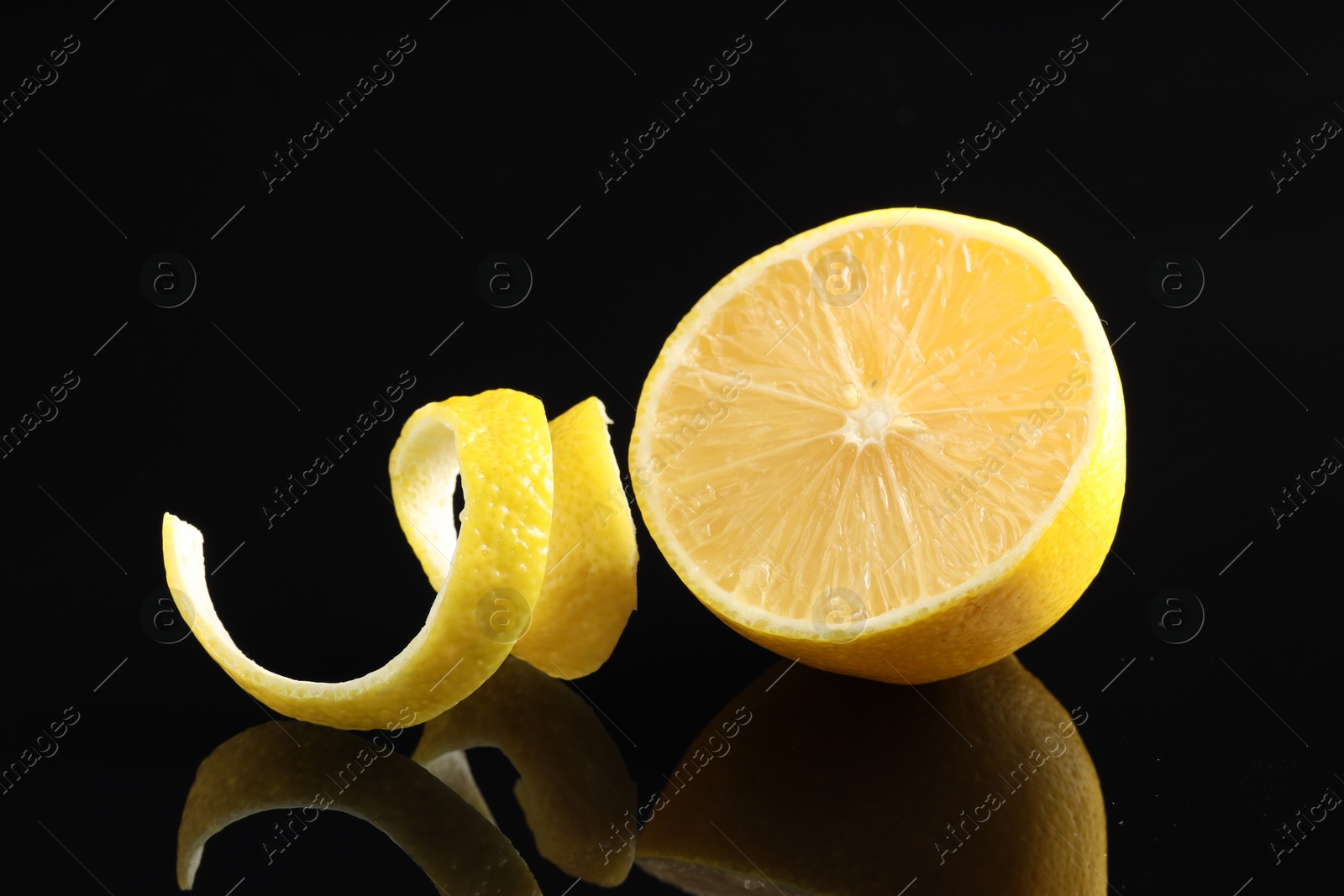 Photo of Fresh lemon peel and half of fruit on black glass surface, closeup