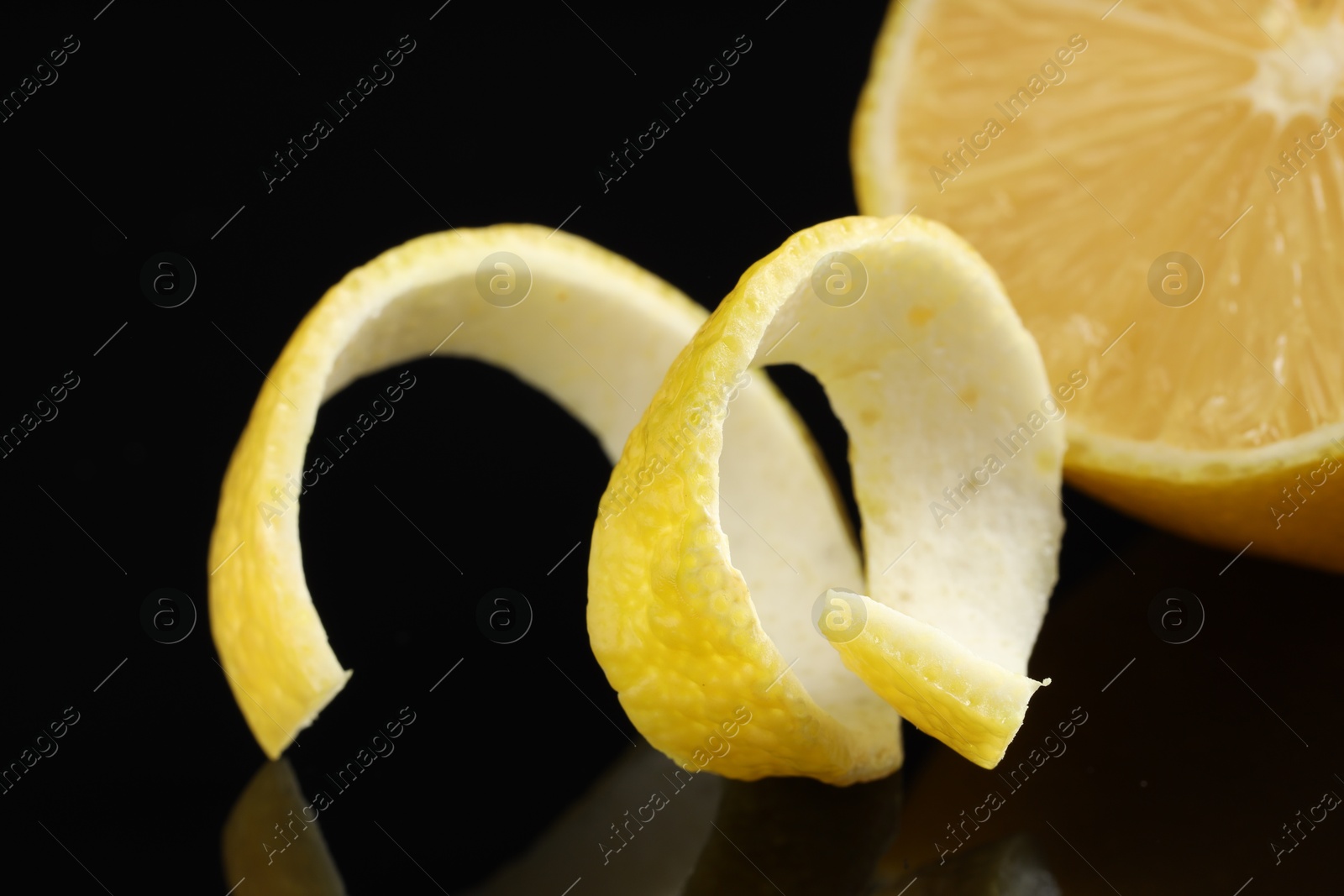 Photo of Fresh lemon peel and fruit on black glass surface, closeup