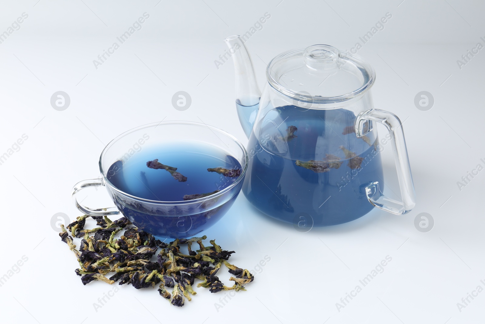 Photo of Delicious butterfly pea flower tea in glass cup, teapot and dry petals on white table