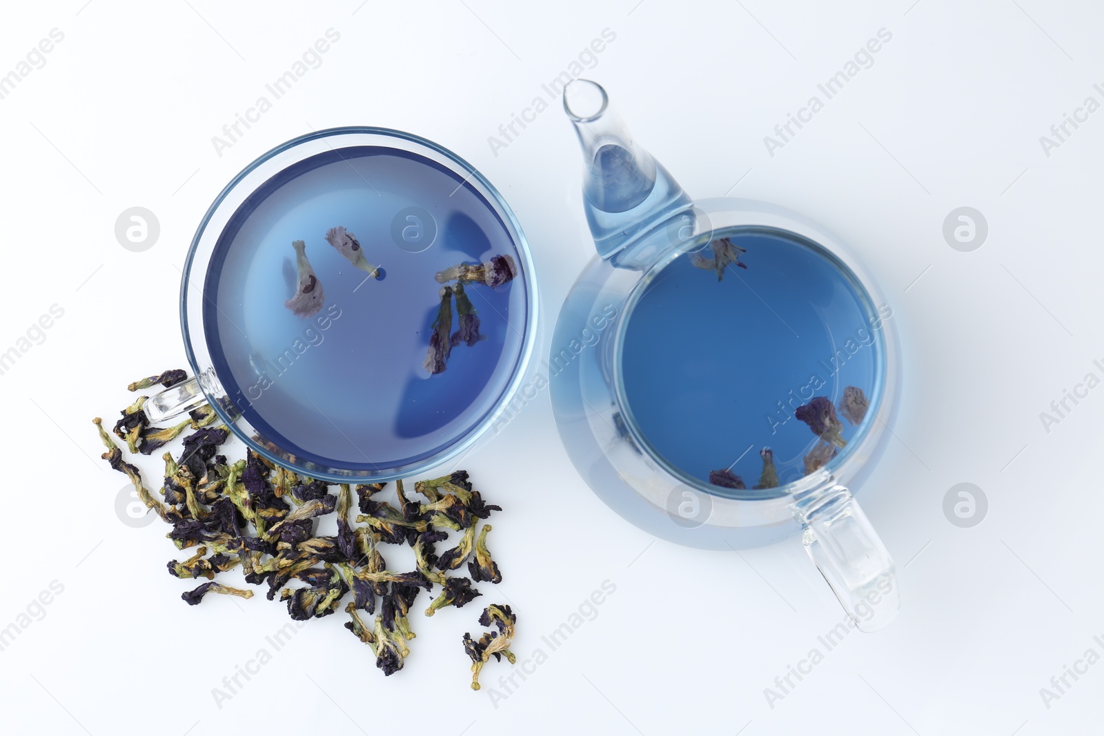 Photo of Delicious butterfly pea flower tea in glass cup, teapot and dry petals on white table, flat lay