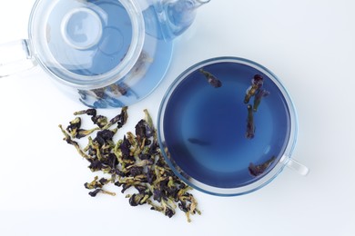 Photo of Delicious butterfly pea flower tea in glass cup, teapot and dry petals on white table, flat lay