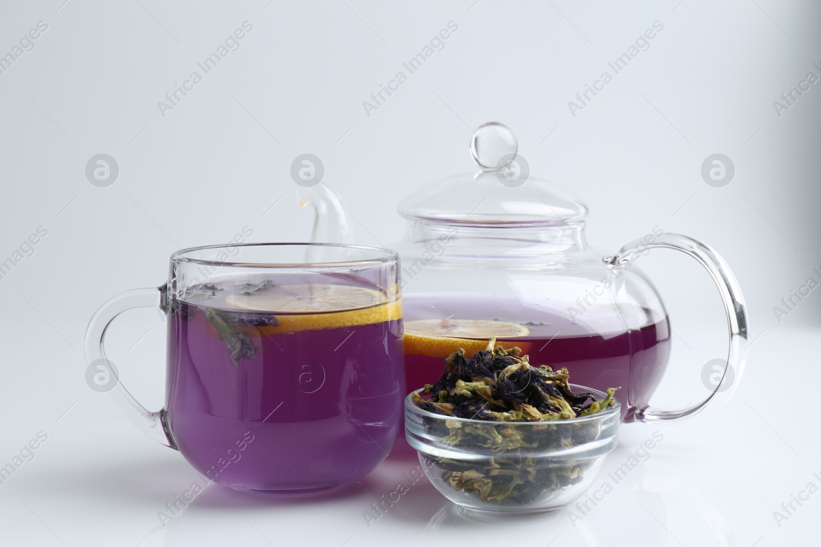 Photo of Delicious butterfly pea flower tea with lemon, teapot and dry petals on white table