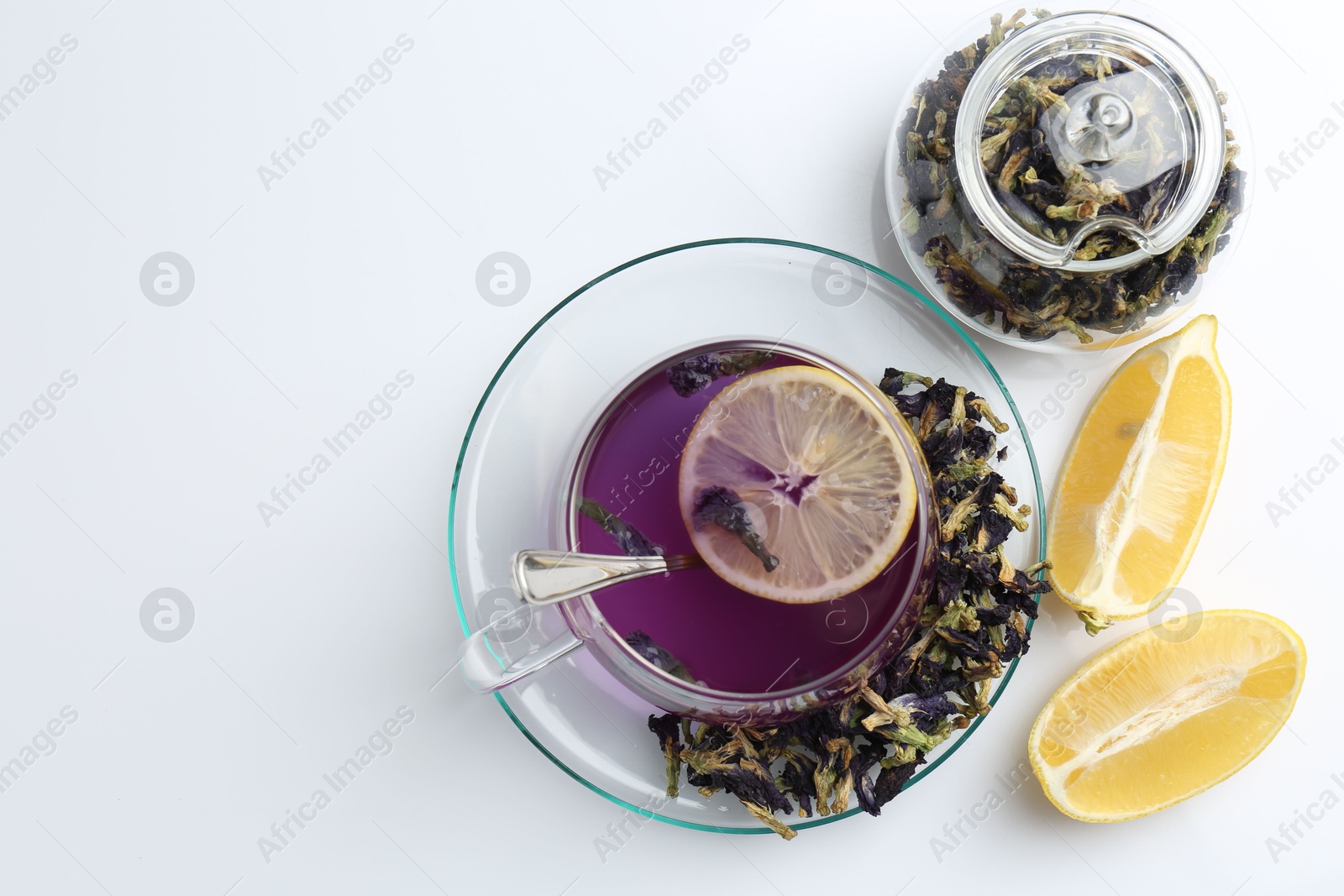 Photo of Delicious butterfly pea flower tea in glass cup, lemon and dry petals on white table, flat lay. Space for text