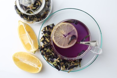 Photo of Delicious butterfly pea flower tea in glass cup, lemon and dry petals on white table, flat lay