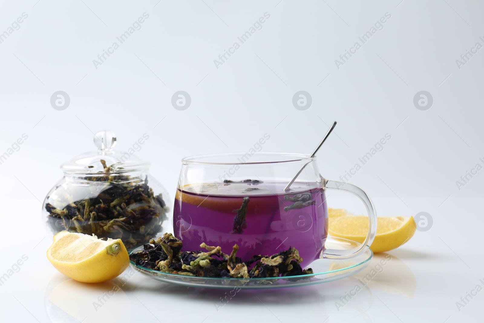 Photo of Delicious butterfly pea flower tea in glass cup, lemon and dry petals on white table