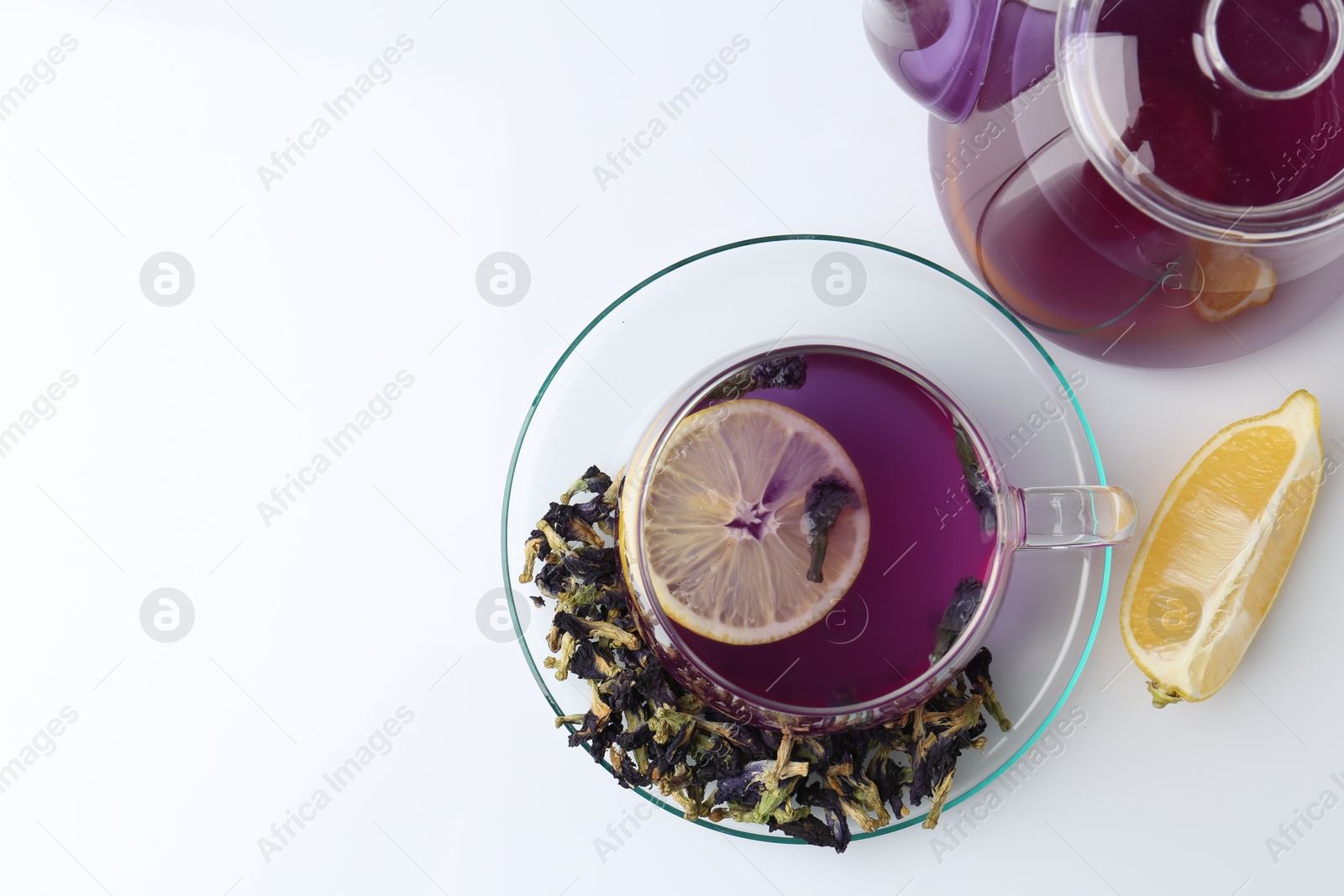 Photo of Delicious butterfly pea flower tea in glass cup, lemon, teapot and dry petals on white table , flat lay. Space for text