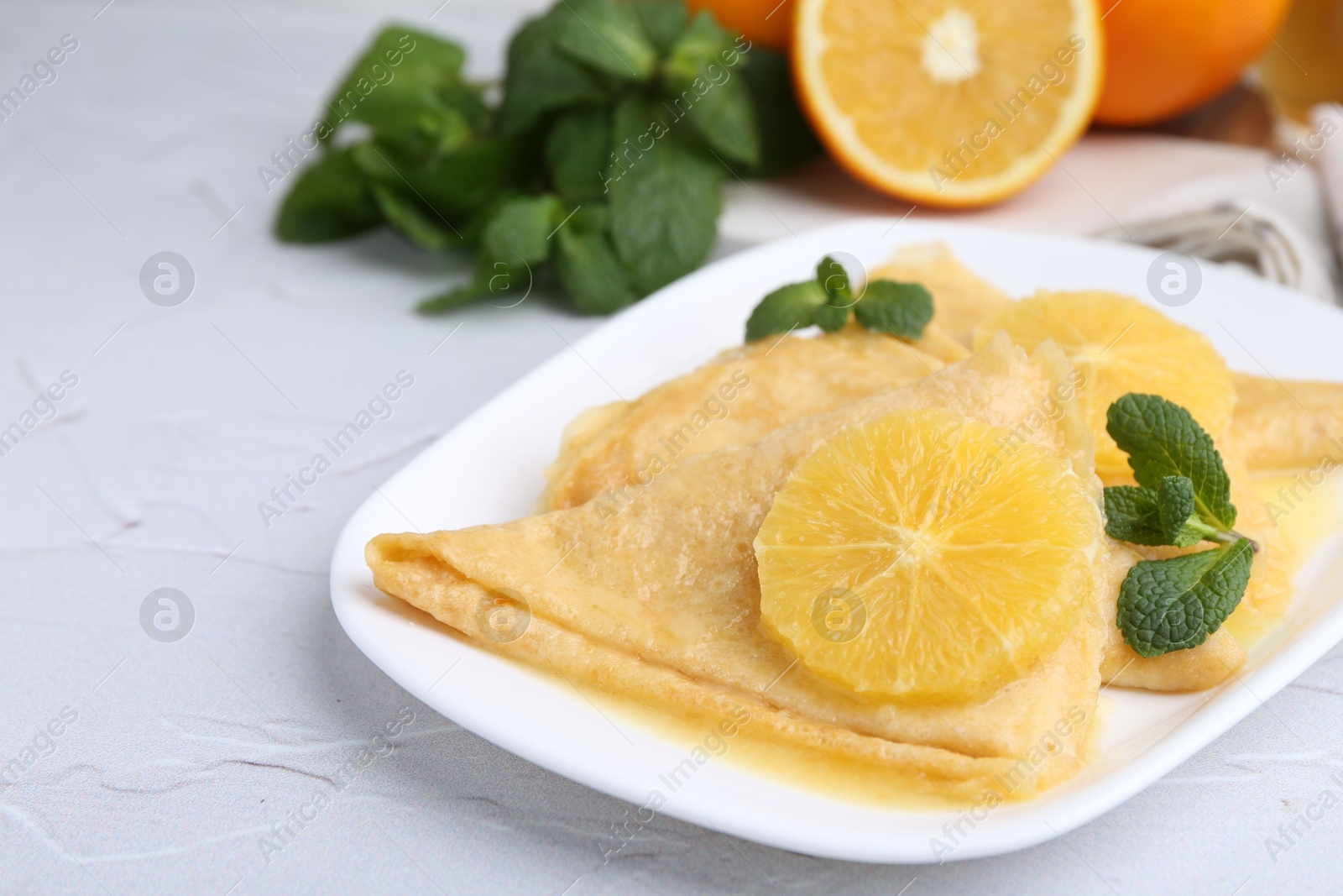 Photo of Delicious Crepes Suzette, mint and oranges on white textured table, closeup