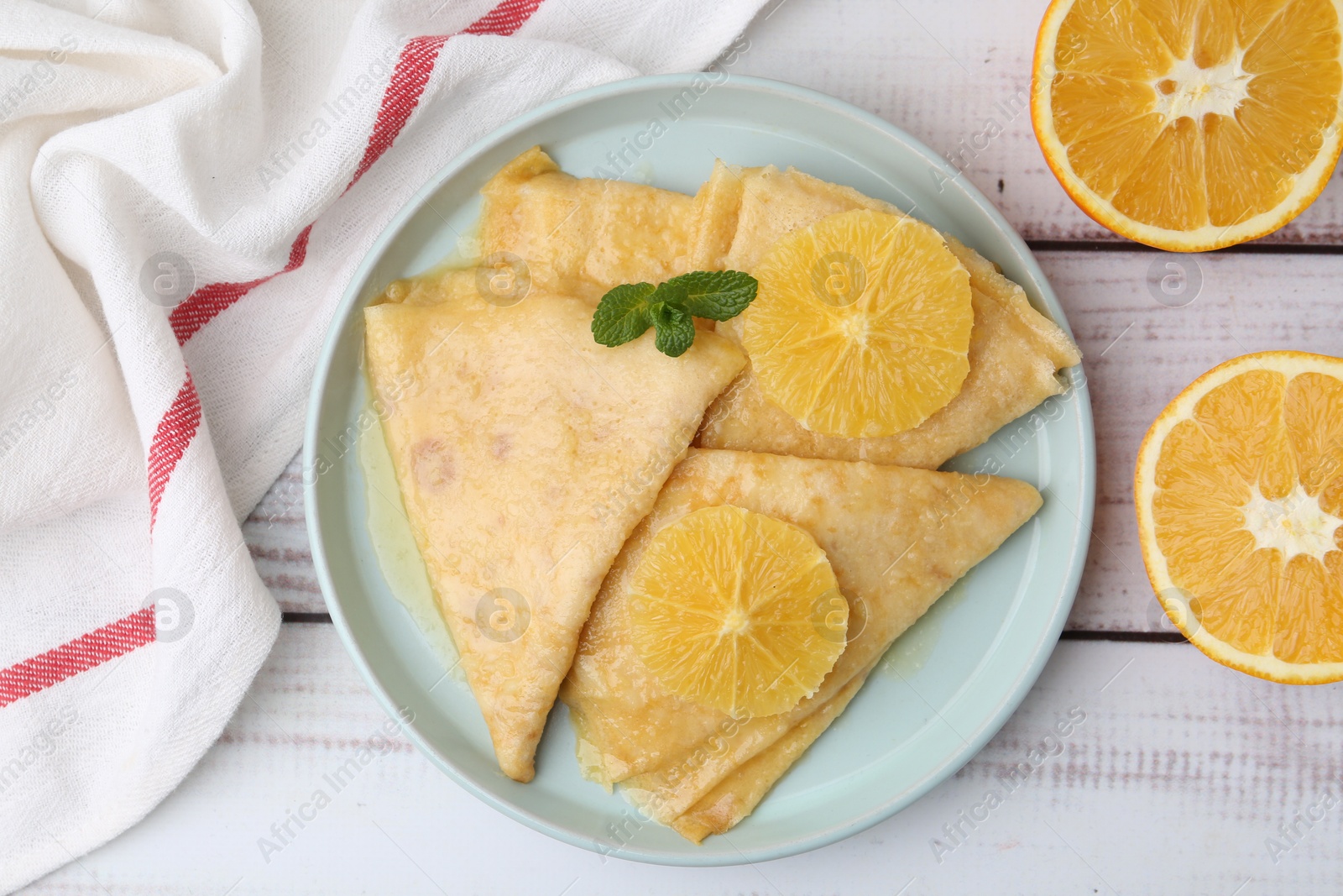 Photo of Delicious Crepes Suzette and oranges on white wooden table, top view