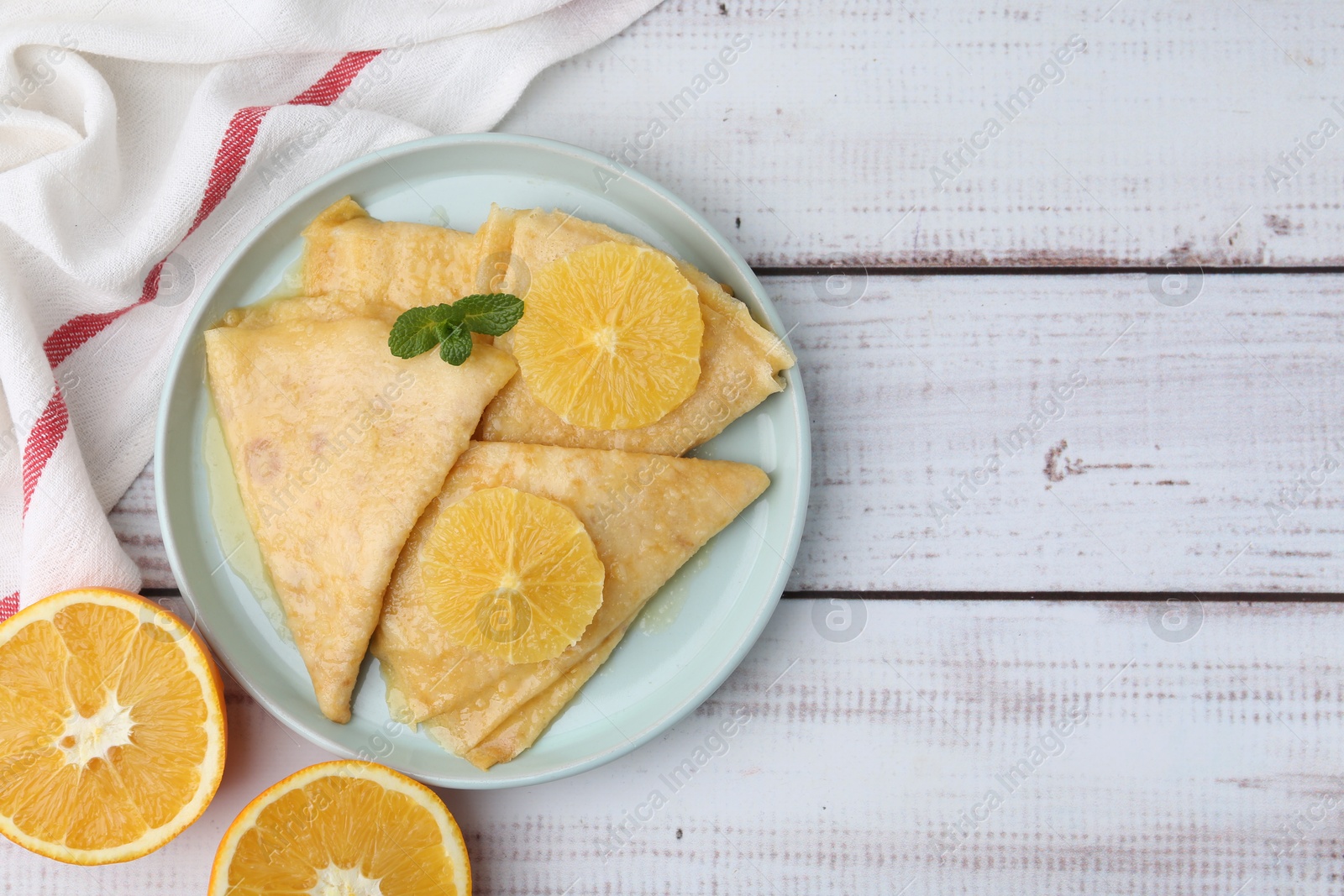 Photo of Delicious Crepes Suzette and oranges on white wooden table, top view. Space for text