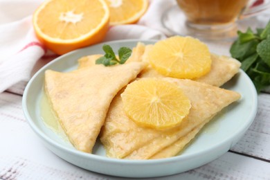 Photo of Delicious Crepes Suzette, mint, tea and oranges on white wooden table, closeup