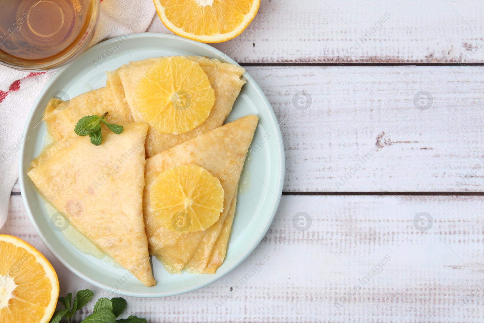 Photo of Delicious Crepes Suzette, tea and oranges on white wooden table, flat lay. Space for text