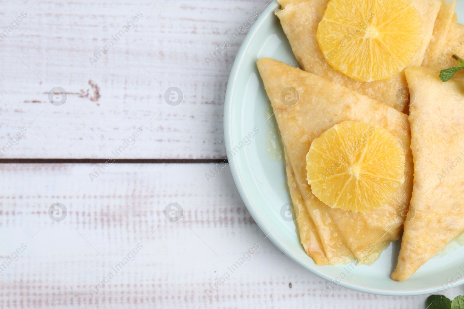 Photo of Delicious Crepes Suzette on white wooden table, top view. Space for text