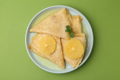 Photo of Delicious Crepes Suzette on green background, top view