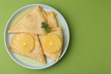 Photo of Delicious Crepes Suzette on green background, top view. Space for text