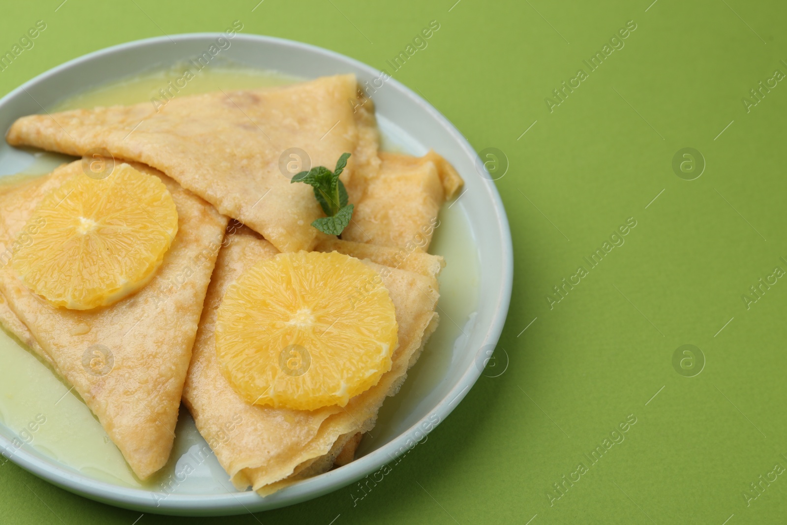 Photo of Delicious Crepes Suzette on green background, closeup