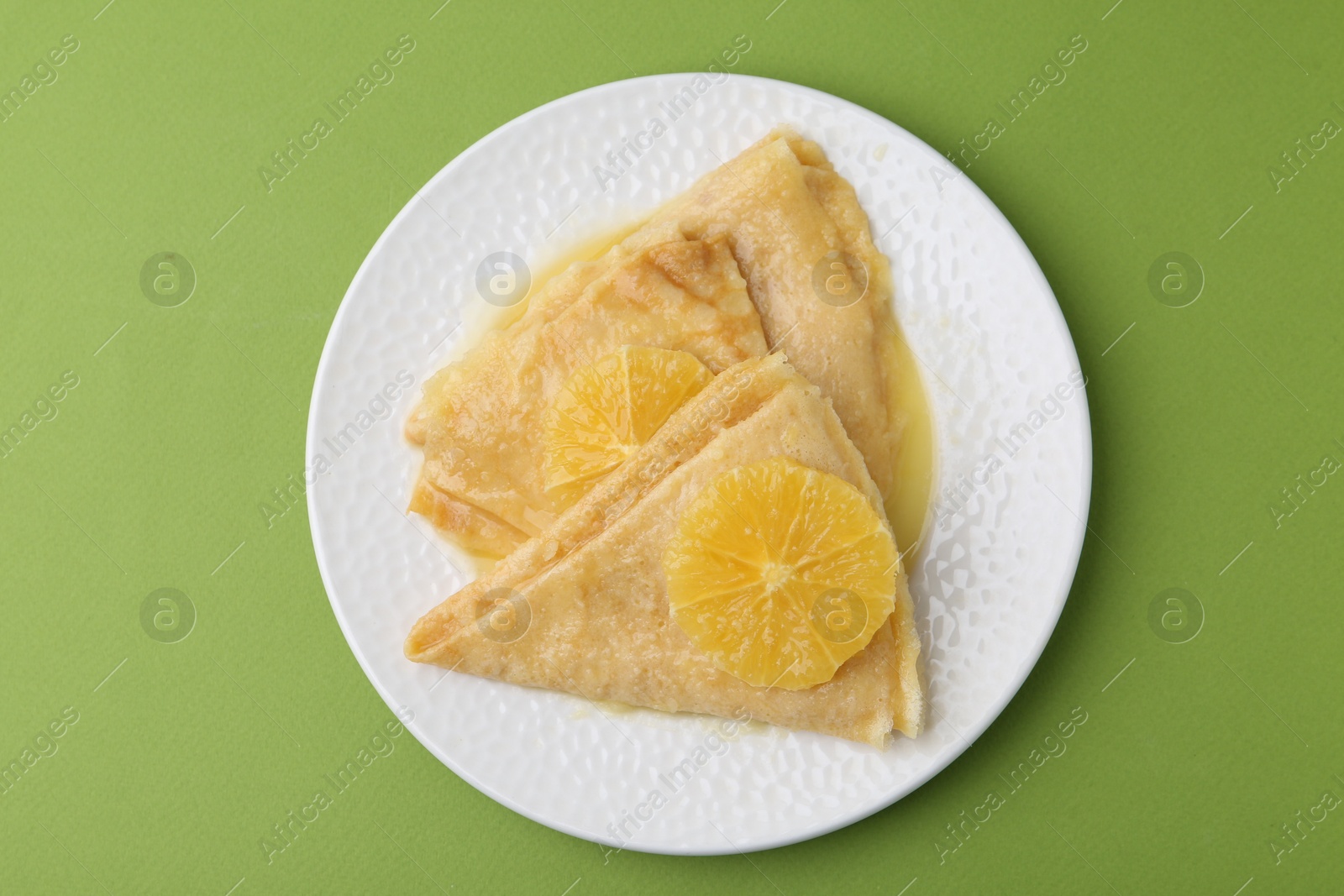 Photo of Delicious Crepes Suzette on green background, top view