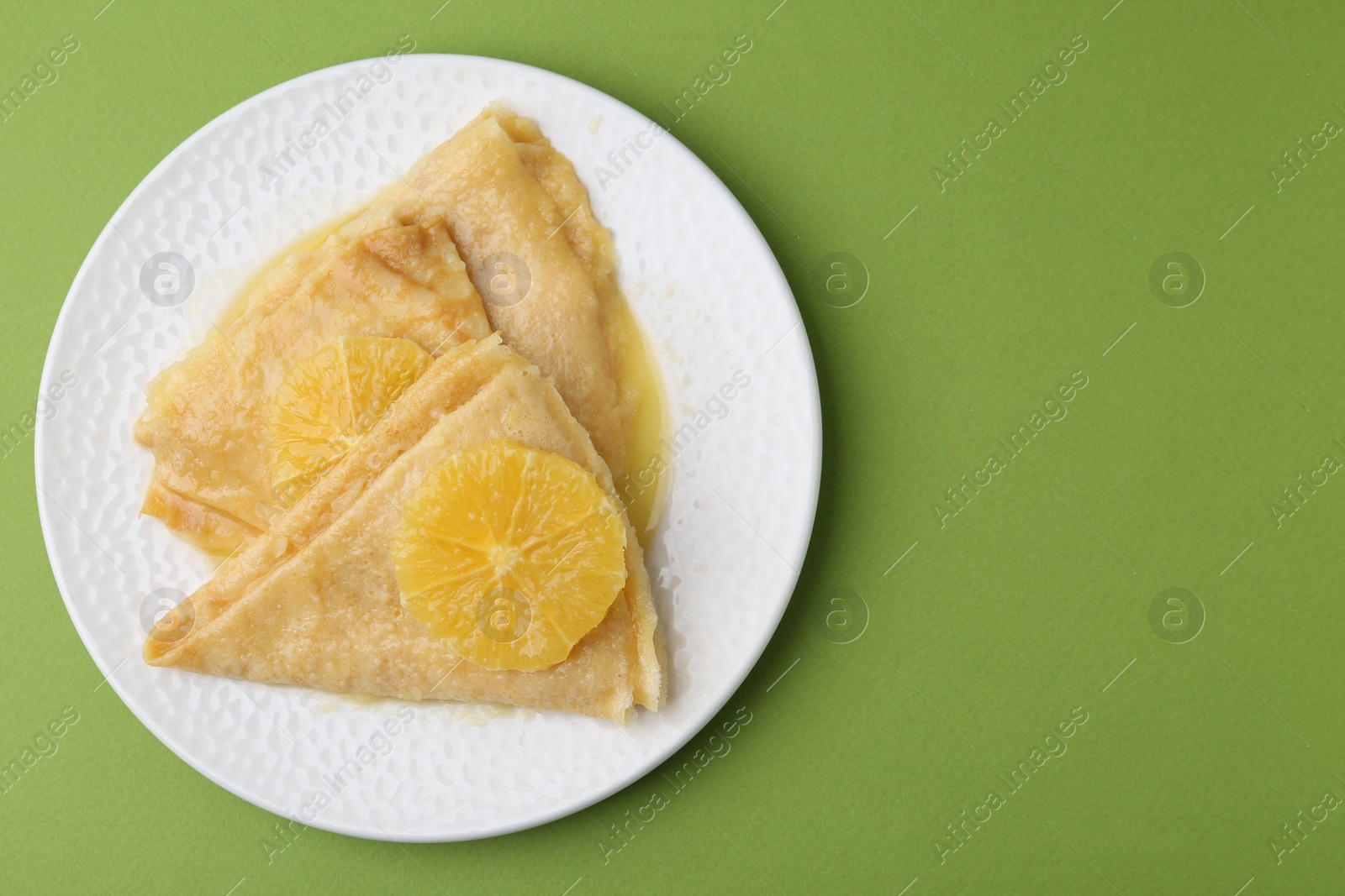 Photo of Delicious Crepes Suzette on green background, top view. Space for text