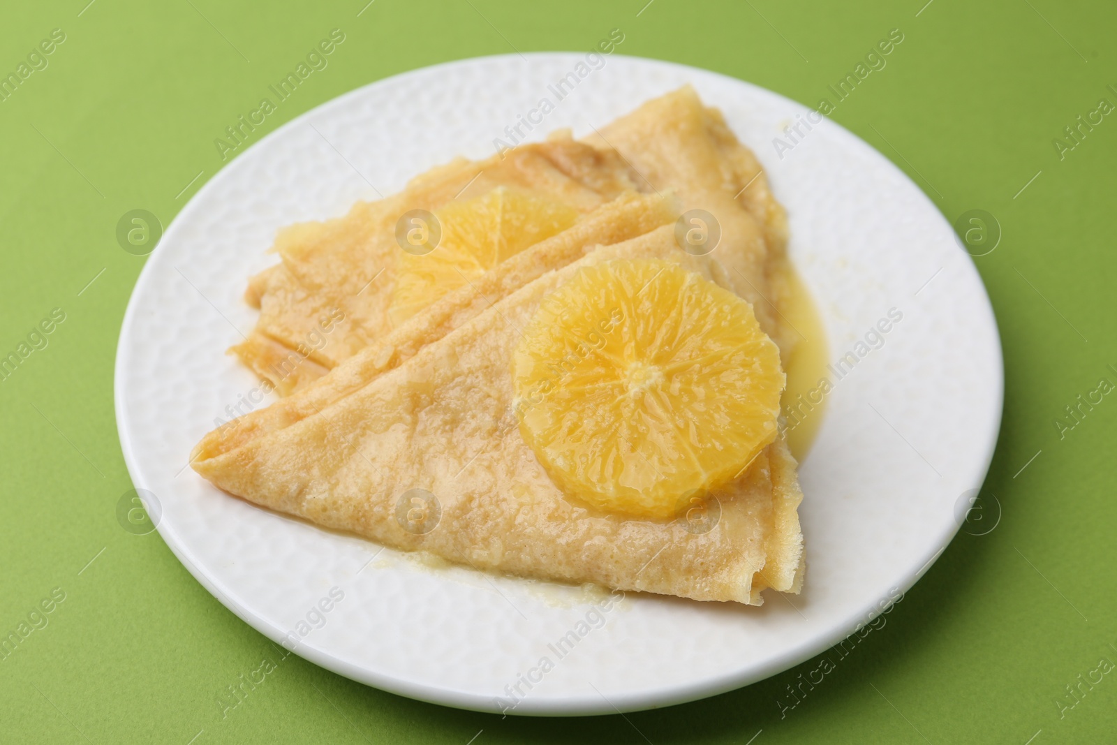 Photo of Delicious Crepes Suzette on green background, closeup