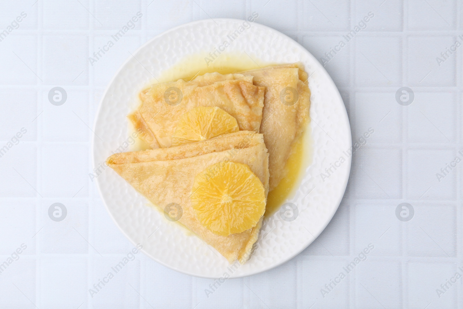 Photo of Delicious Crepes Suzette on white tiled table, top view