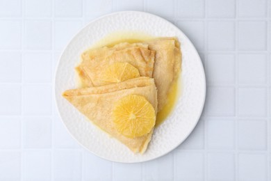 Photo of Delicious Crepes Suzette on white tiled table, top view