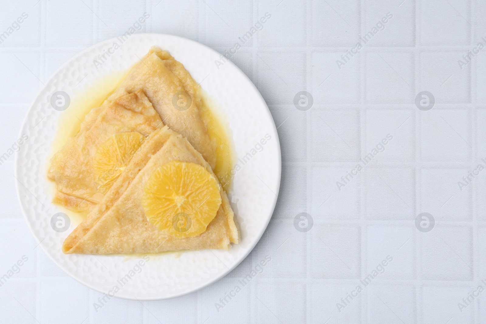 Photo of Delicious Crepes Suzette on white tiled table, top view. Space for text