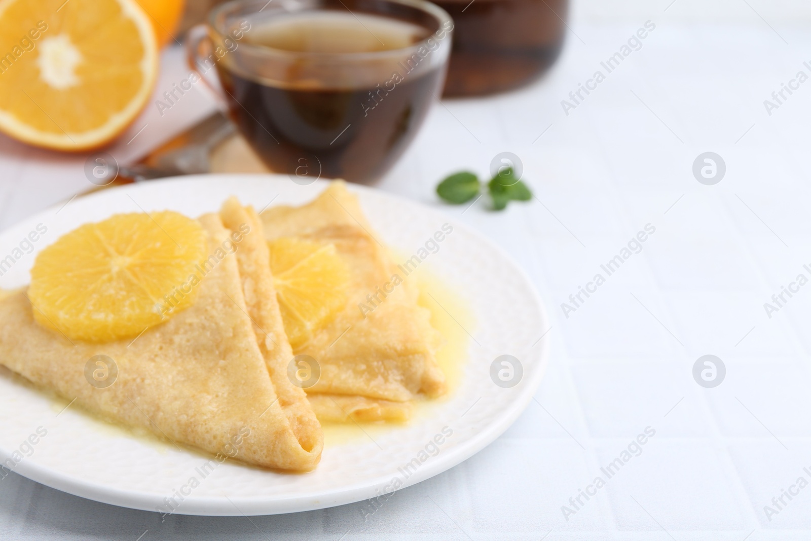 Photo of Delicious Crepes Suzette served on white tiled table, closeup. Space for text