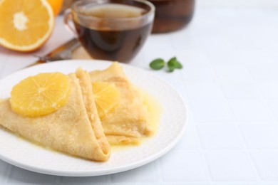 Photo of Delicious Crepes Suzette served on white tiled table, closeup. Space for text