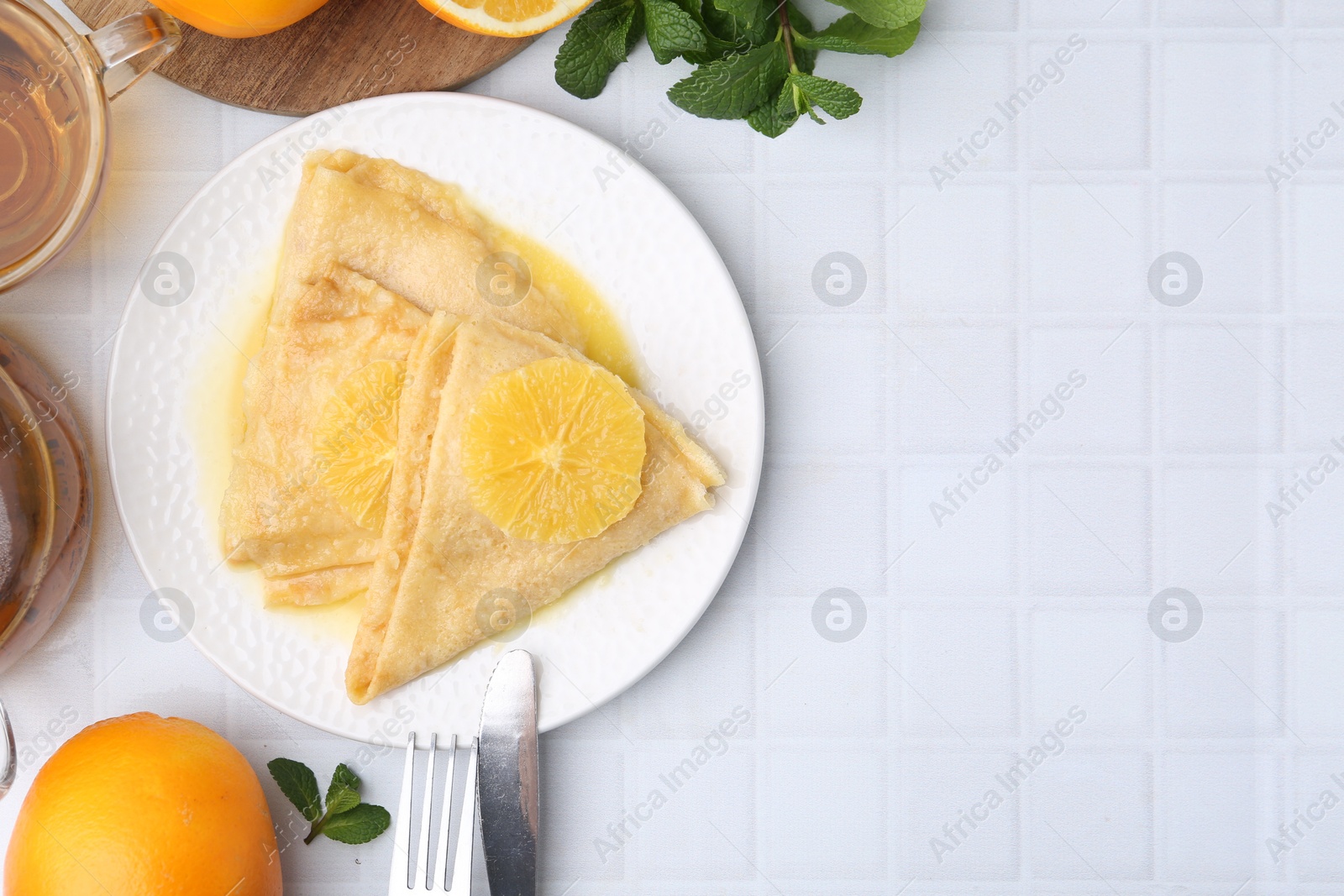 Photo of Delicious Crepes Suzette served on white tiled table, flat lay. Space for text