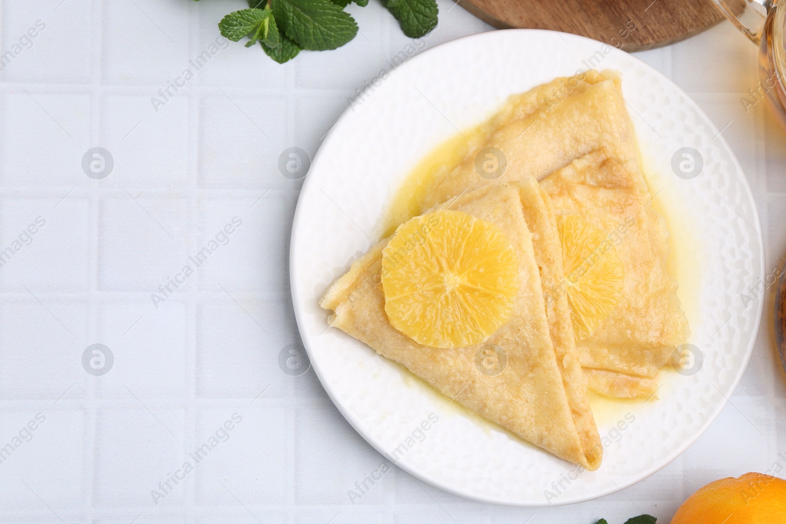 Photo of Delicious Crepes Suzette on white tiled table, top view. Space for text