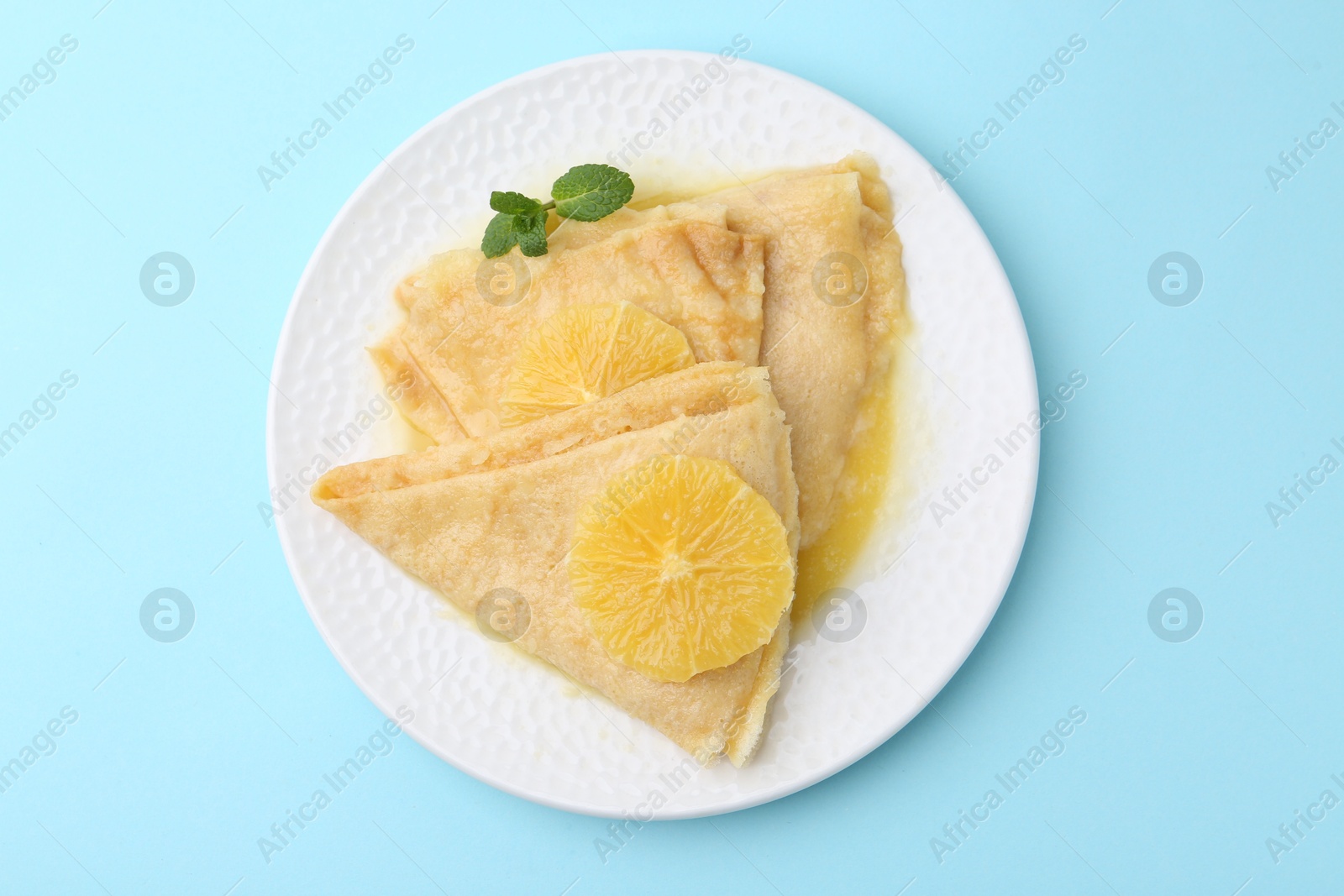 Photo of Delicious Crepes Suzette on light blue background, top view