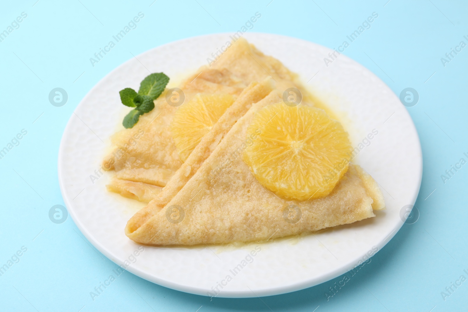 Photo of Delicious Crepes Suzette on light blue background, closeup