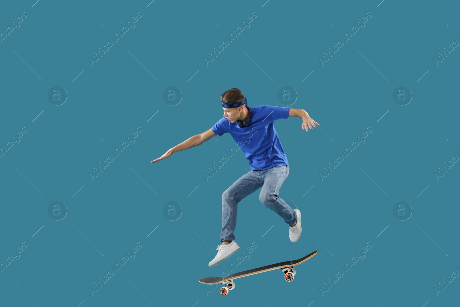 Image of Handsome man with skateboard in air on blue background. Performing trick