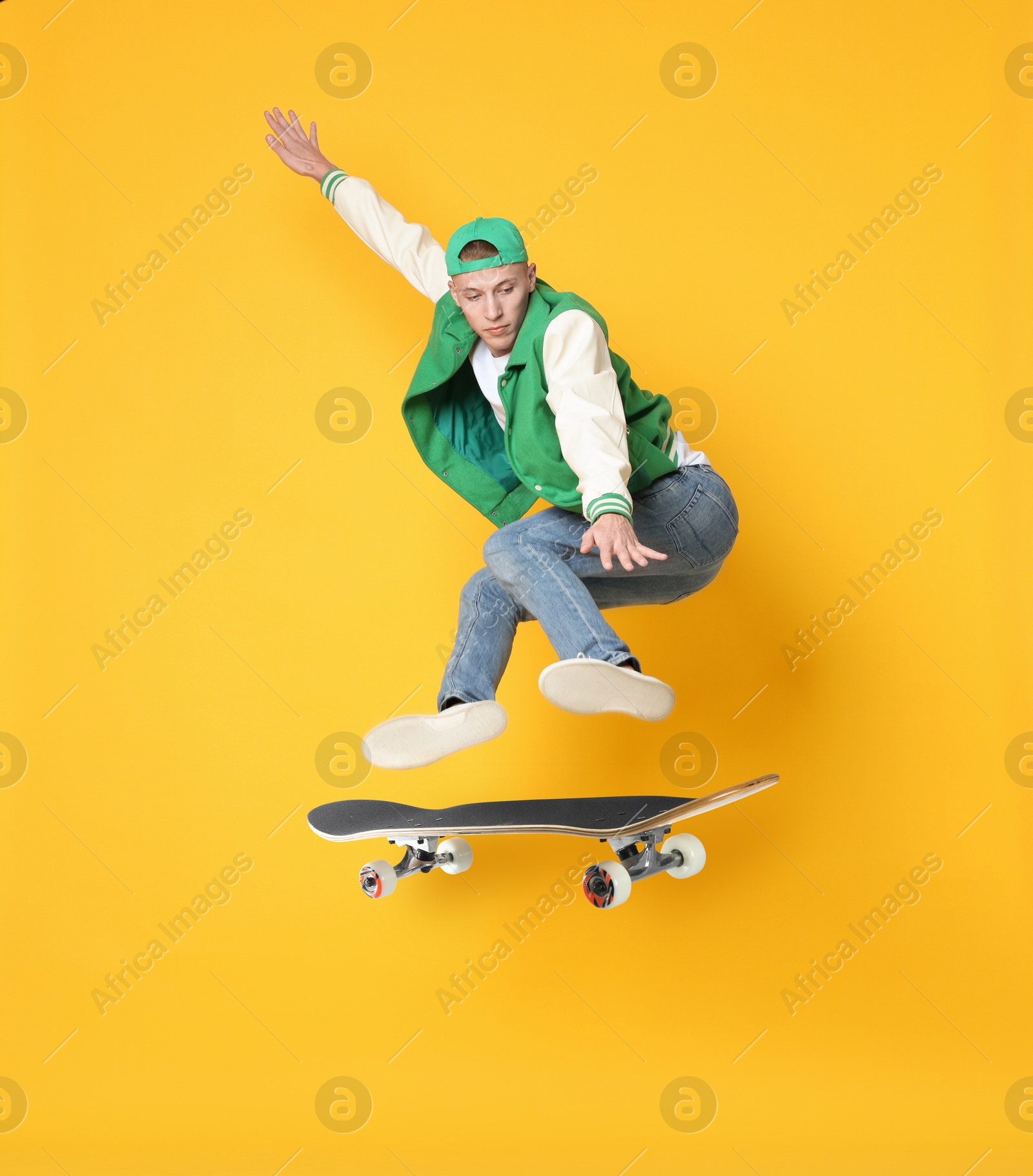 Image of Handsome man with skateboard in air on orange background. Performing trick