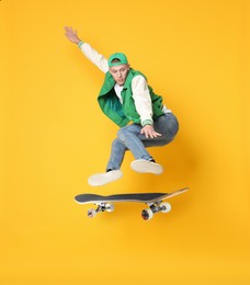 Image of Handsome man with skateboard in air on orange background. Performing trick